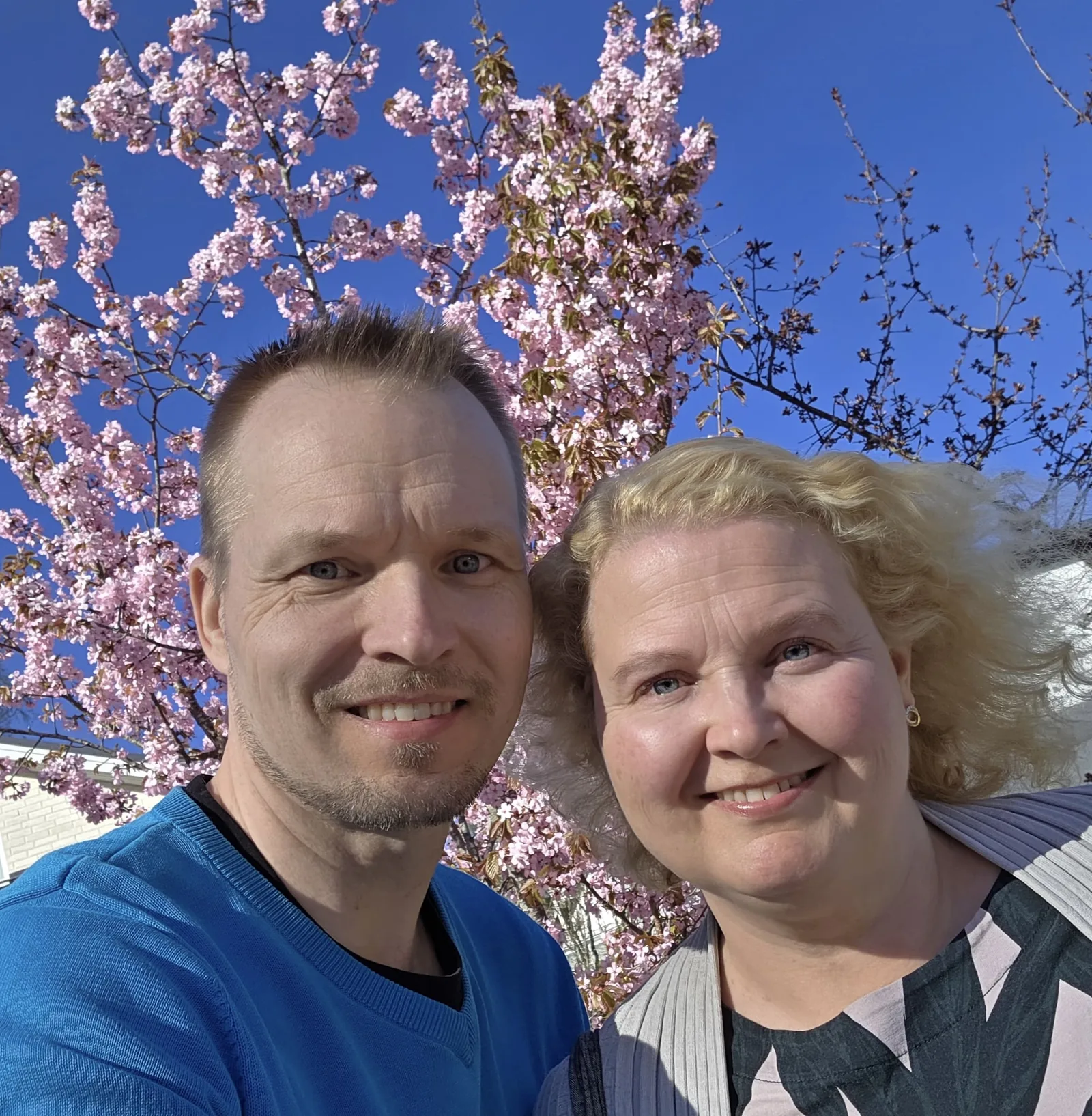Marjo ja Pekka kevätauringossa kirsikkapuun edessä