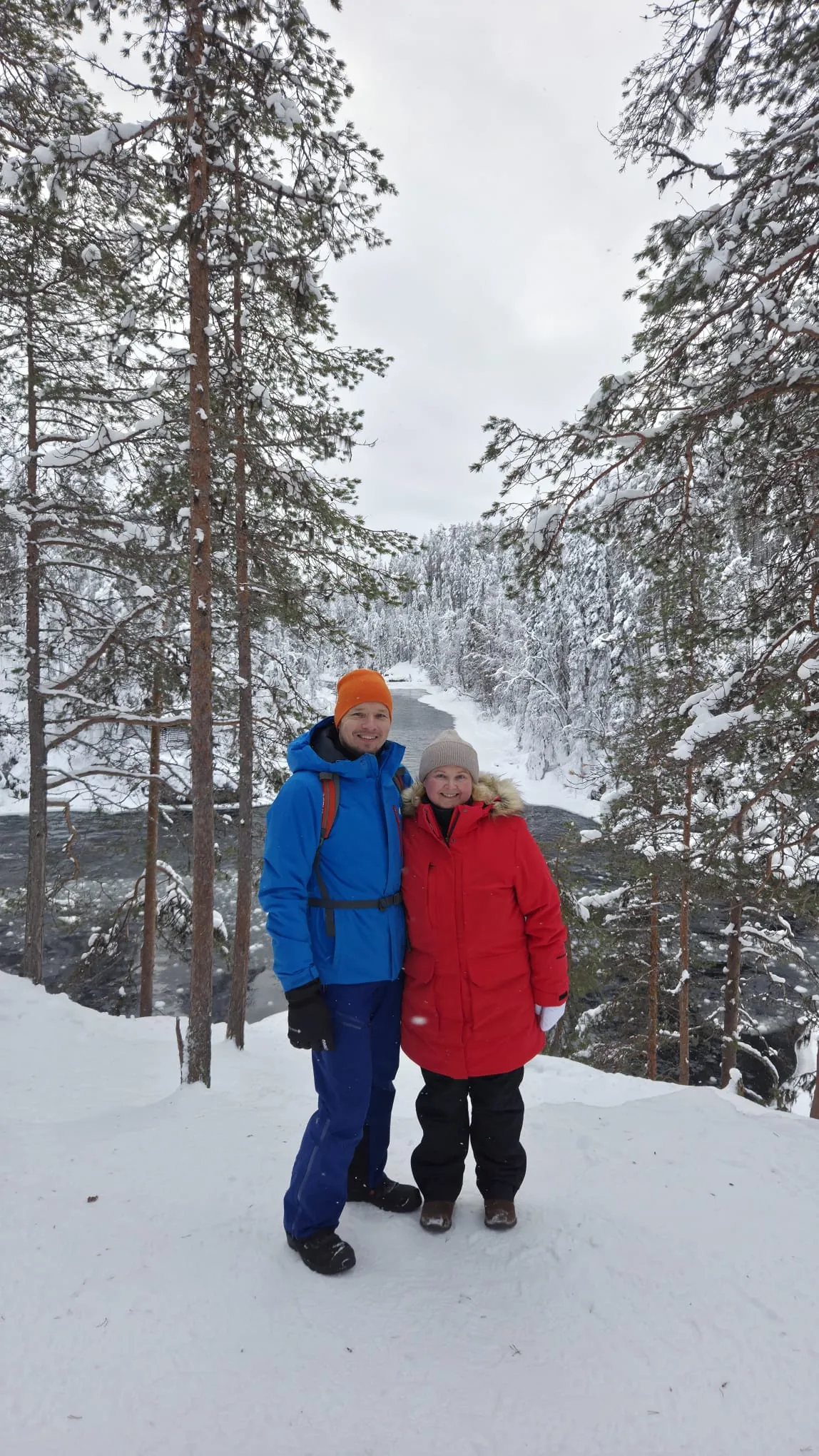 Marjo ja Pekka talvella lumisessa metsässä jokimaiseman äärellä